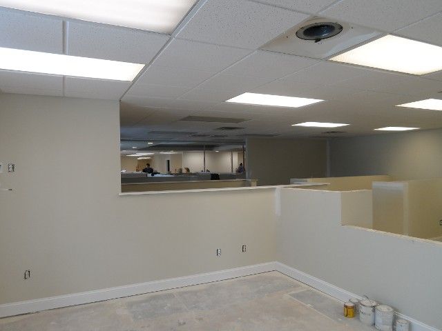 Interior view of an office space with cubicles, a lowered wall, and ceiling lights.