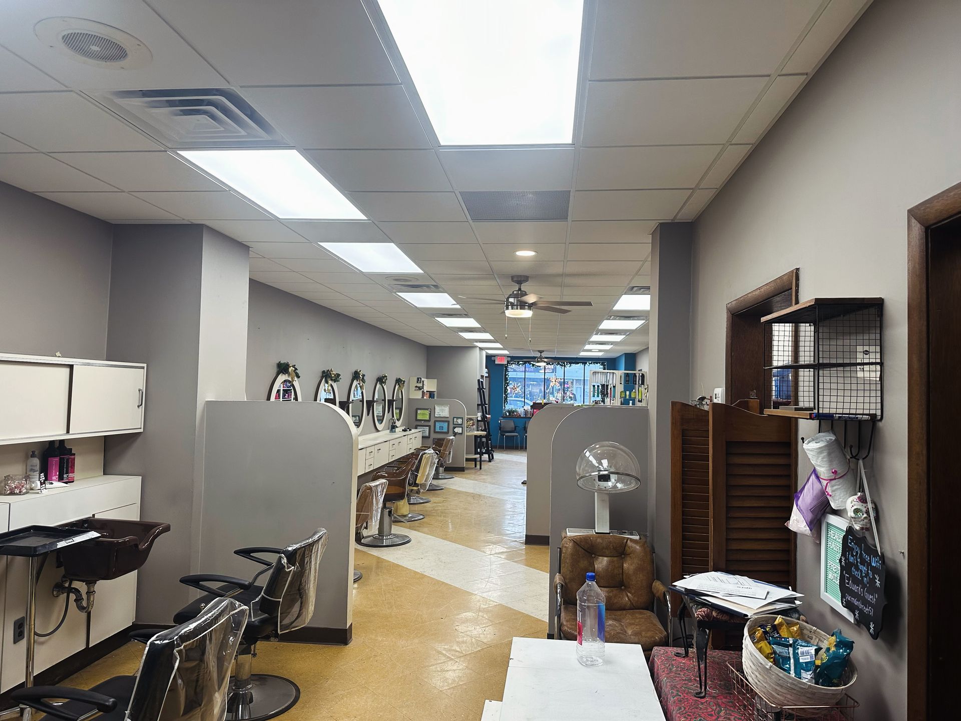 Interior of a hair salon with rows of styling stations, mirrors, and chairs. Neutral walls, bright overhead lighting.