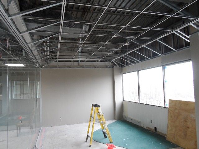 Interior room under construction with metal ceiling framework, drywall, and a ladder.