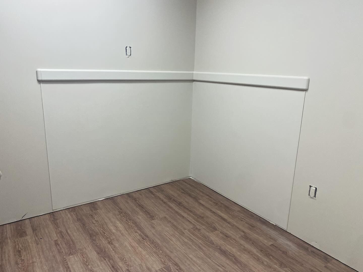 Corner of a room with light wood-look flooring and white walls. A white ledge runs along the wall.