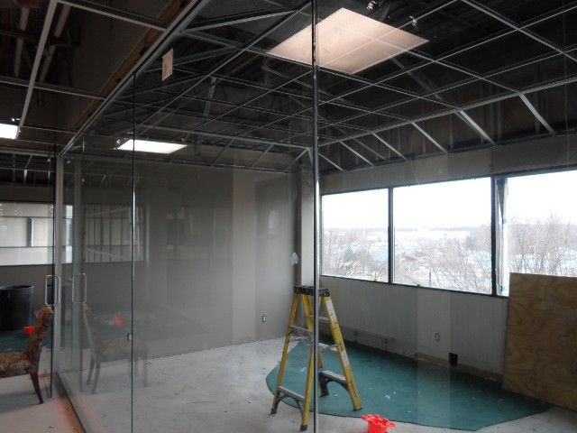 Interior construction site with glass office walls, windows, and a yellow ladder.