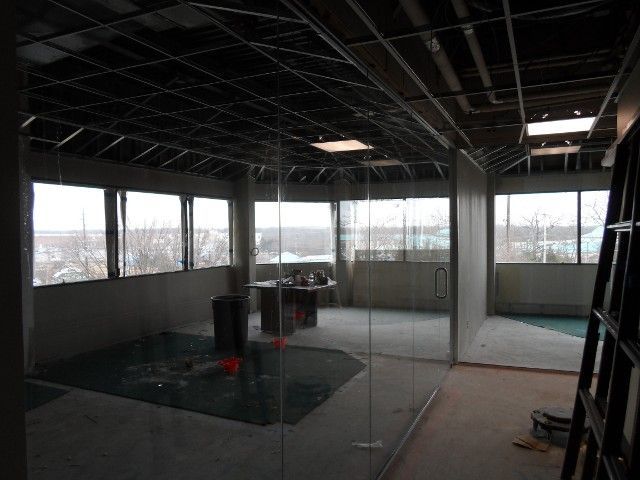Interior of a room under construction, with exposed ceiling beams, windows, and glass walls.