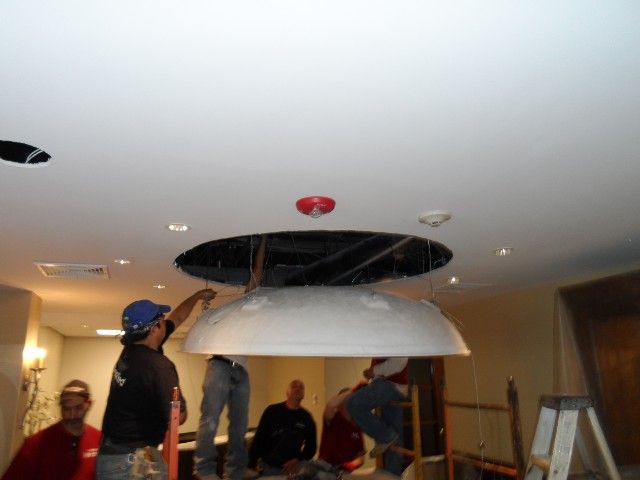 Workers installing a large, white dome ceiling fixture. They are standing on ladders and looking up.
