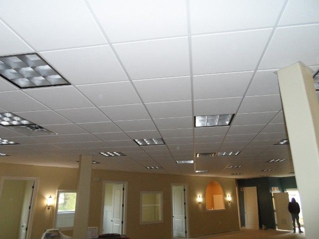 White tiled ceiling with recessed lights in a large room, beige walls, several doorways.