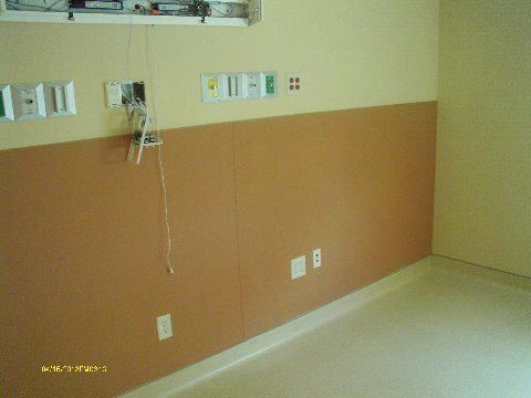Empty hospital room with brown wainscoting and tan upper walls. Electrical outlets and medical ports visible.