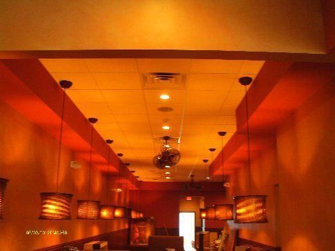 Restaurant interior with orange walls and ceiling, pendant lights hanging, and a fan.