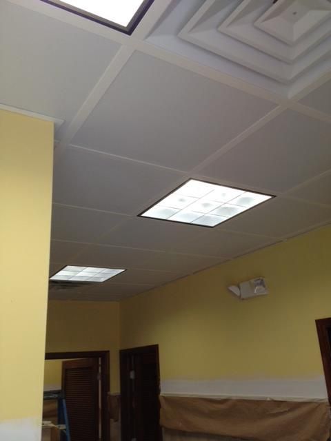 A low-angle view of a room with a drop ceiling, fluorescent lights, and yellow walls.
