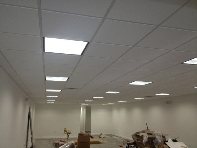 White office ceiling with recessed fluorescent lights. Empty room with white walls and construction debris.