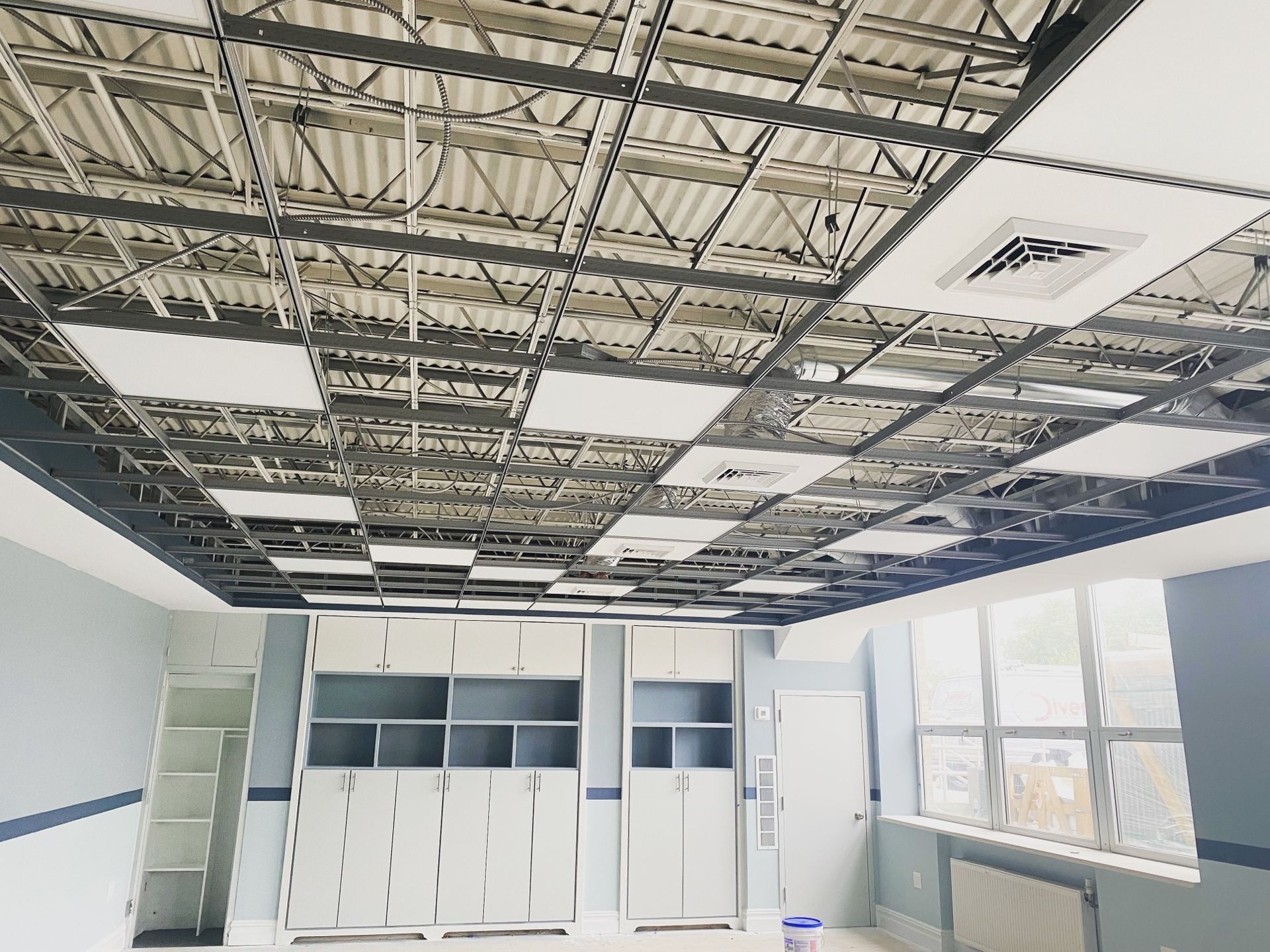 Interior view of a room with a metal ceiling grid, cabinets, a door, and a window.