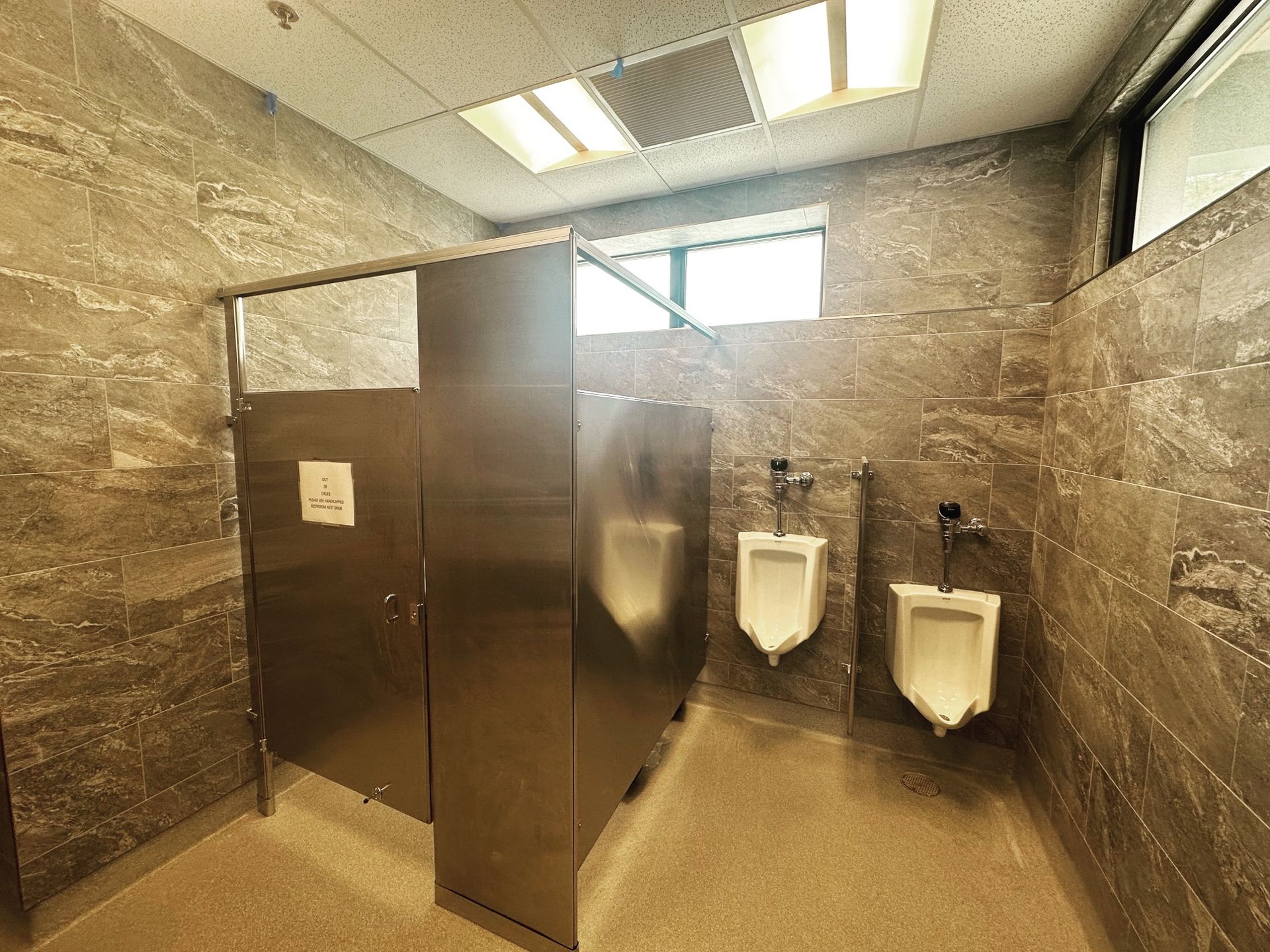 Public restroom with stainless steel stalls and urinals, tile walls and floor.