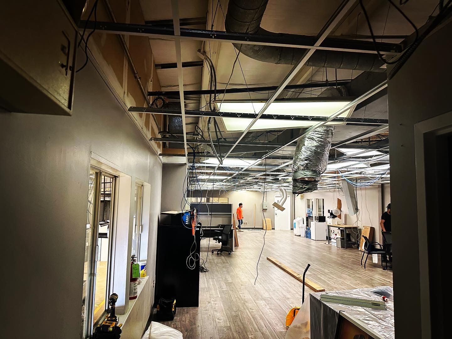 Interior view of a room under construction with exposed ceiling elements, a worker, and unfinished walls.