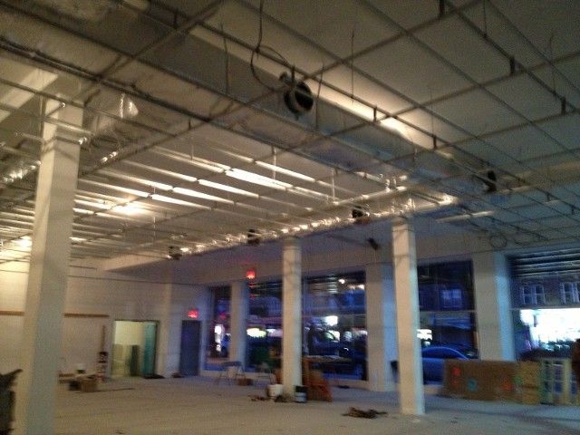 Interior of a large commercial space under construction with exposed beams, columns, and a partially finished ceiling.