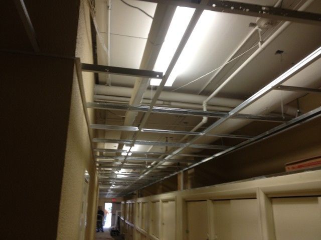 Hallway ceiling with exposed metal framing, fluorescent lights, and closed doors along the wall.