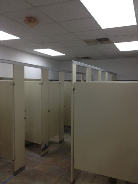 Public restroom stalls with cream-colored doors and dividers, under white ceiling lights.