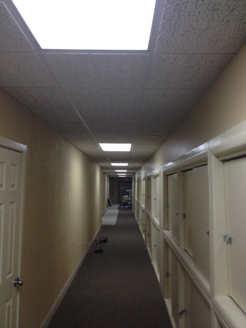 Long, empty hallway with doors on the right and a drop ceiling.