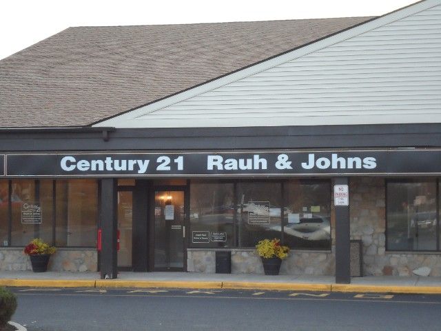 Century 21 Rauh & Johns office building with storefront windows, brown roof, and floral planters.