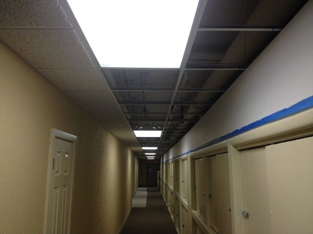 Narrow hallway with tan walls, closed doors, and overhead fluorescent lights.