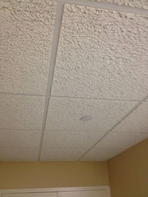 Textured white ceiling tiles with recessed lighting, in a room with light yellow walls.