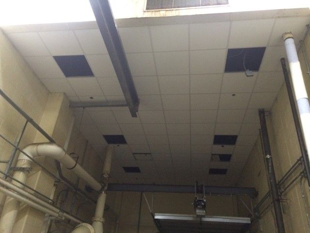 Ceiling with missing tiles, pipes, and beams in an enclosed space.