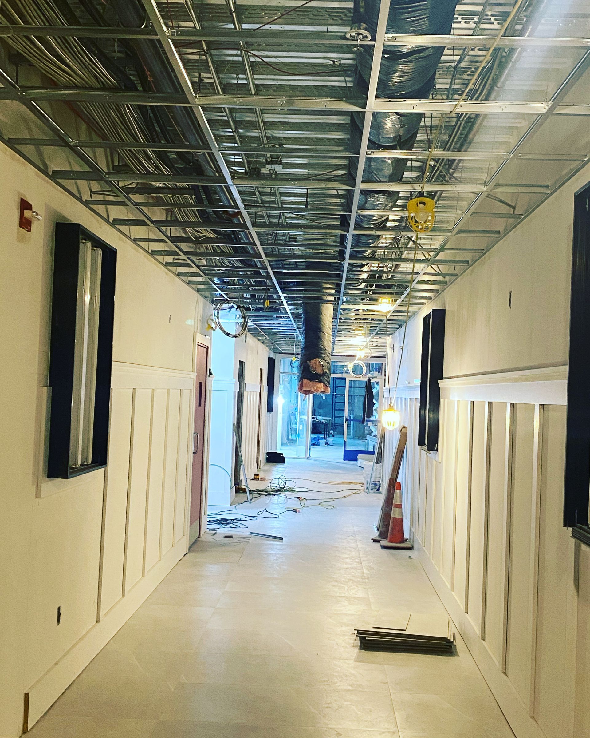 Hallway under construction; metal ceiling framework, drywall, exposed pipes.