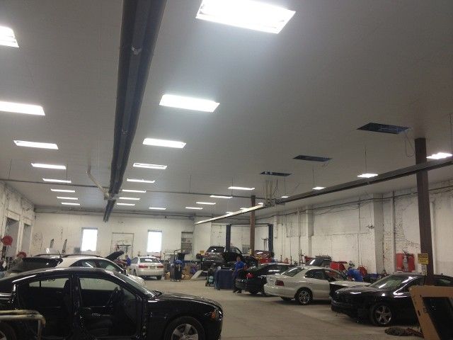 Cars inside a well-lit auto repair shop. Mechanics work on vehicles under fluorescent lights.