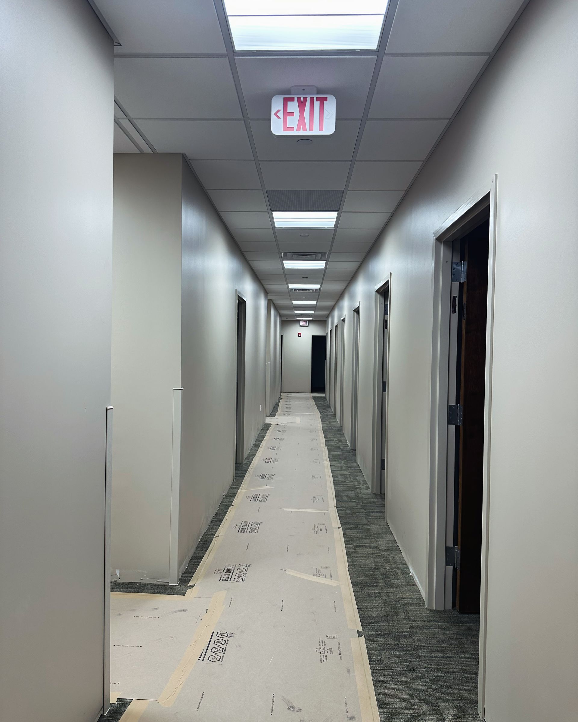 Long hallway with beige walls, doors, and a partial carpet runner. 