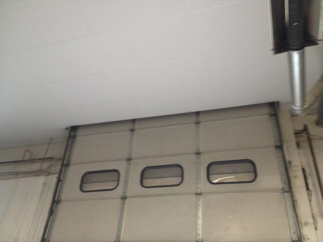 Closed, light-colored industrial garage door with three windows, mounted on a wall; white ceiling overhead.