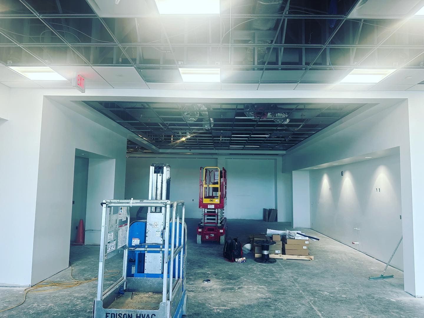 Interior construction site with lift equipment, unfinished walls, and exposed ceiling infrastructure.