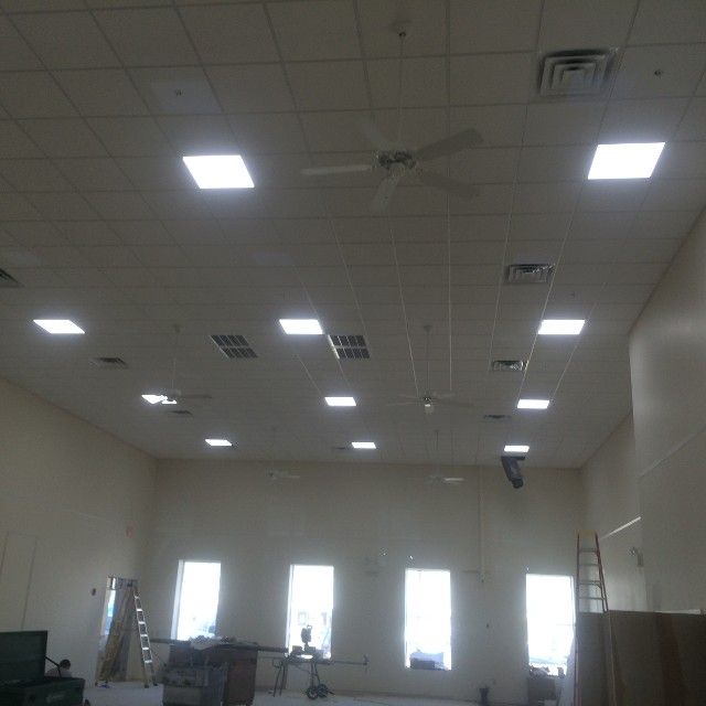 Ceiling with square lights, windows, fans, and drywall in a large, empty room.