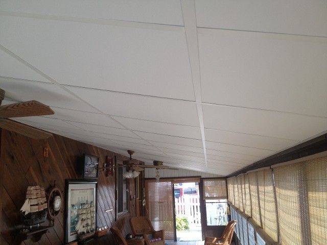 Enclosed porch interior with white ceiling, wooden walls, and open door to the outside.