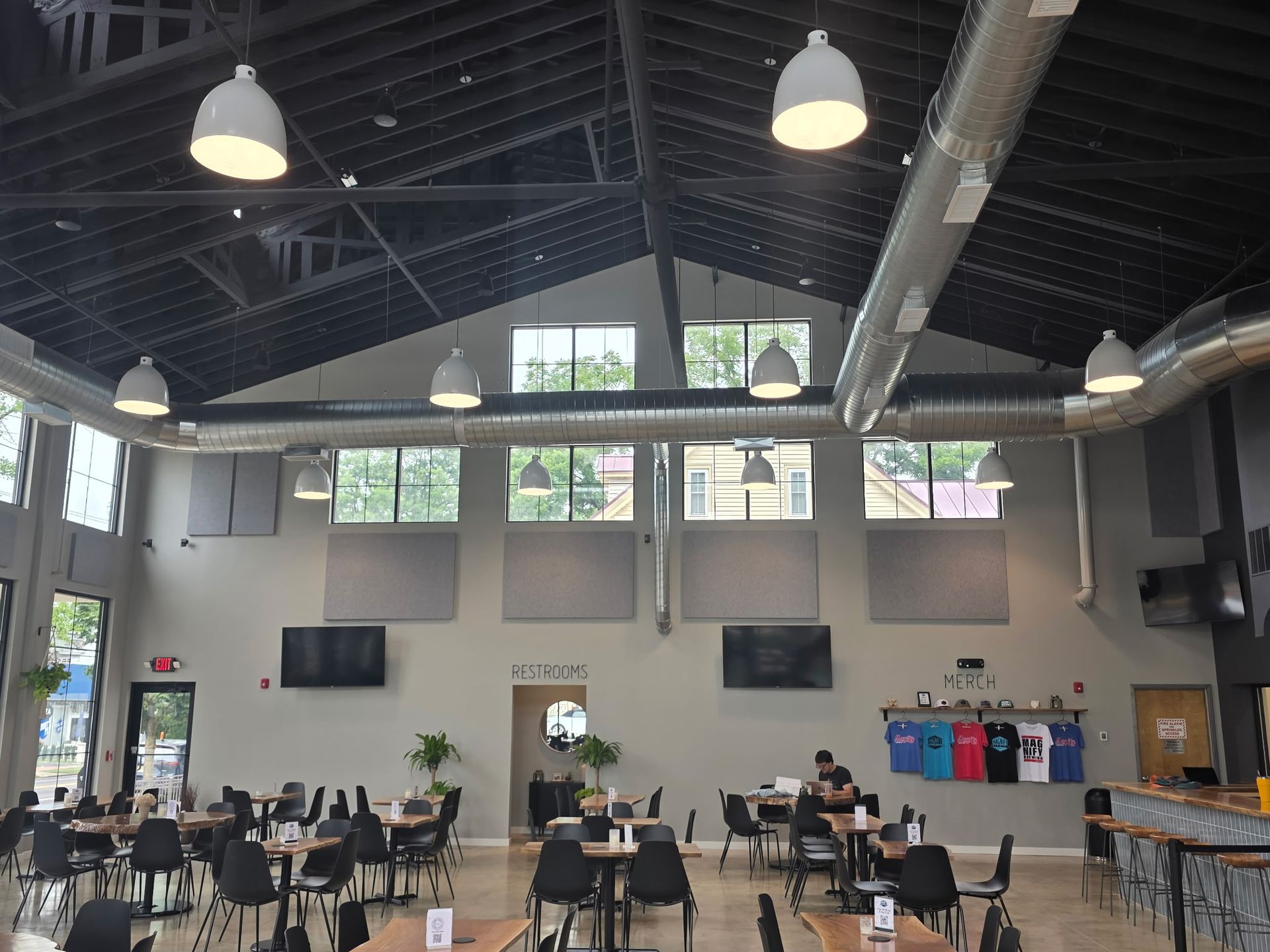 Interior of a brewery. Tables, chairs, and a bar area. Windows high on walls, lights.