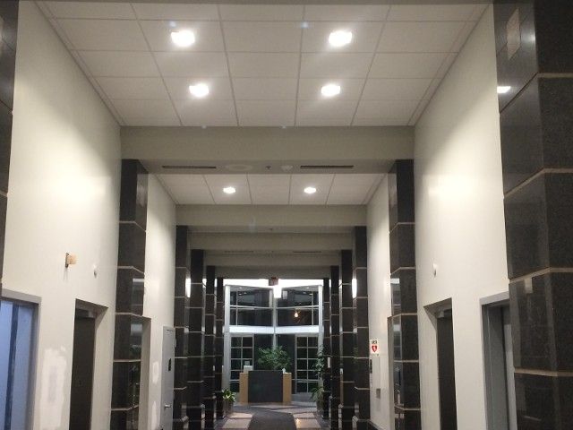 Hallway with white walls, black columns, and recessed lighting leading to a glass door.