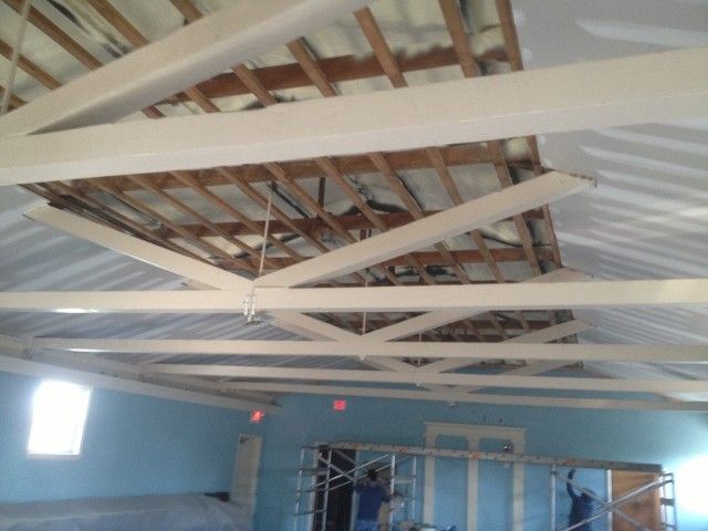 Ceiling with exposed wooden beams, a hole, and workers inside a building.