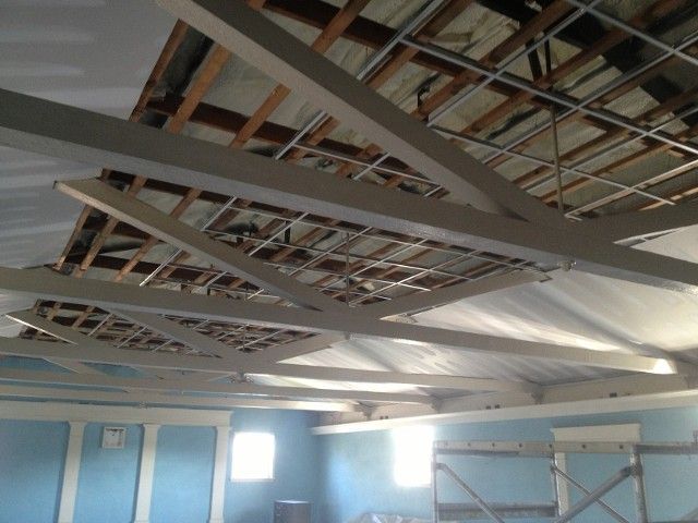 Ceiling with exposed beams, partially removed drywall, showing wooden roof structure and wiring.