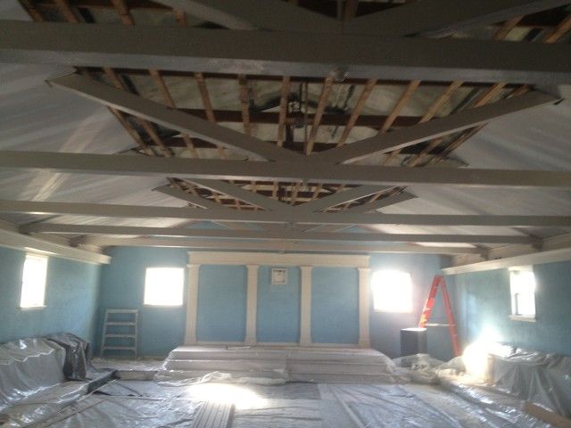 Interior of a room under construction with blue walls, exposed beams, and plastic sheeting on the floor.