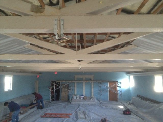 Interior renovation, room with wooden beams and scaffolding. Two workers are present. Blue walls.