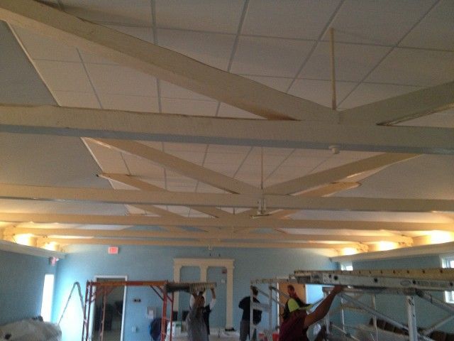 Workers installing a ceiling in a room with light blue walls and decorative wooden beams.