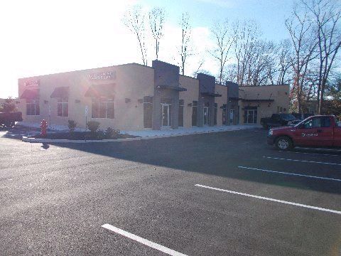 Exterior of a commercial building with a parking lot. Beige walls, gray accents, and a red truck.