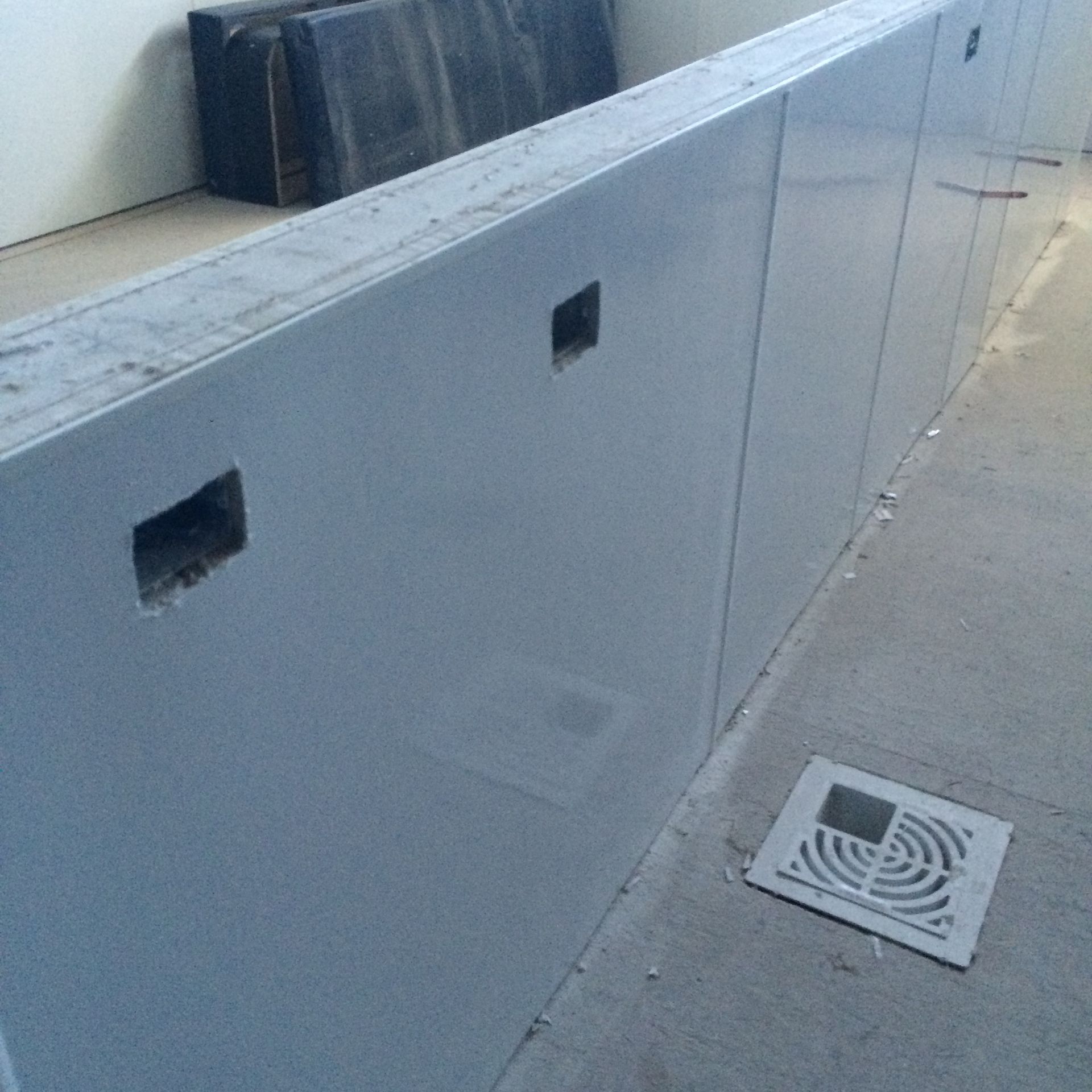 Gray painted concrete wall with square cutouts and a floor drain on a concrete floor.