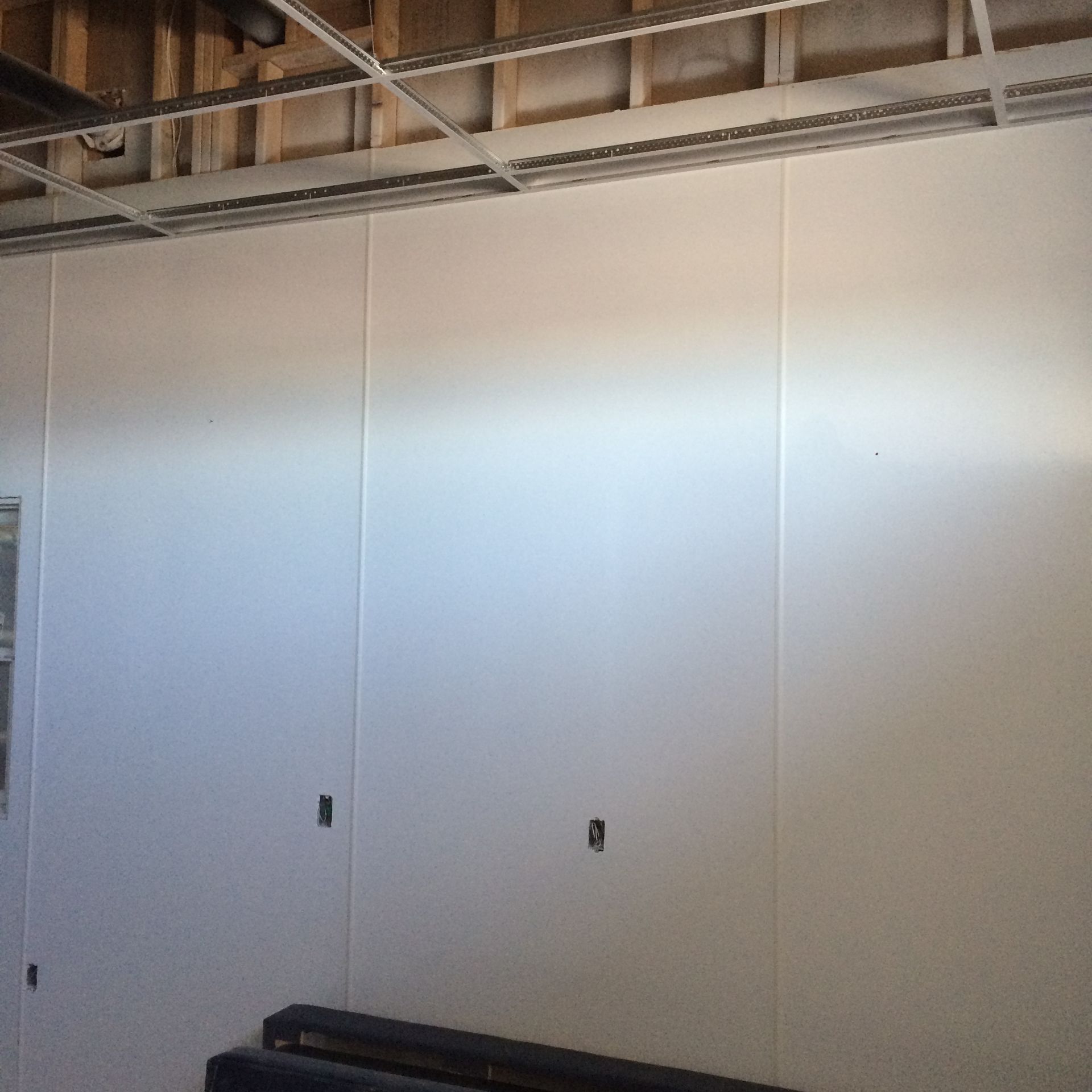 White wall panels in a room under construction, with a partial drop ceiling above.