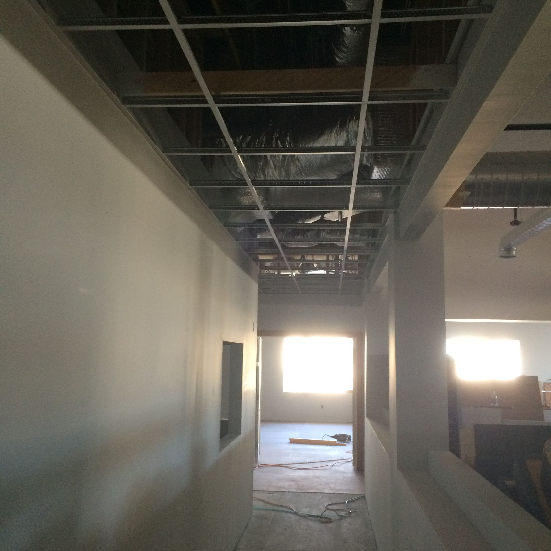 Hallway under construction; metal ceiling frame, unfinished walls, bright windows at end.