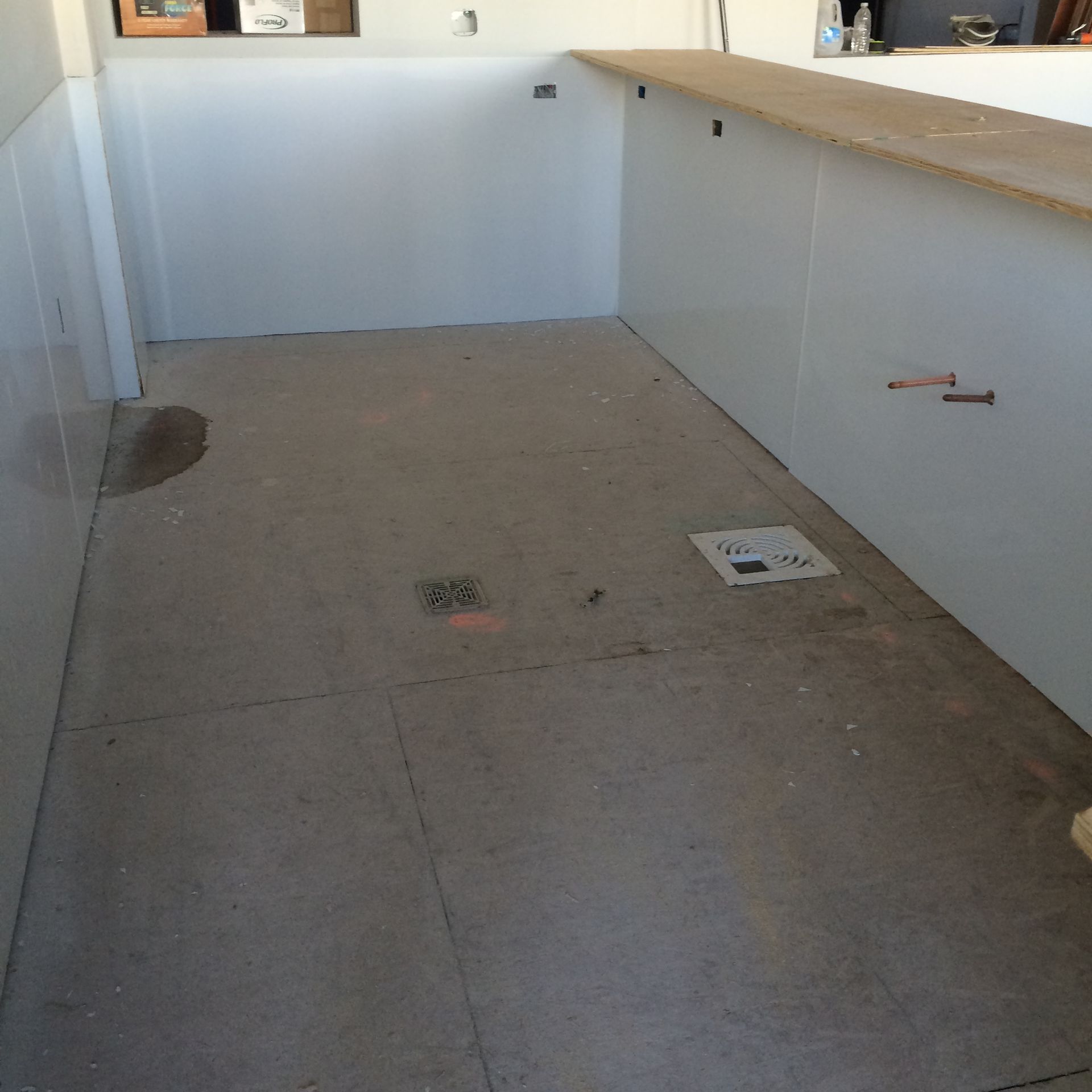 Empty room with concrete floor, white walls, and a wood countertop.