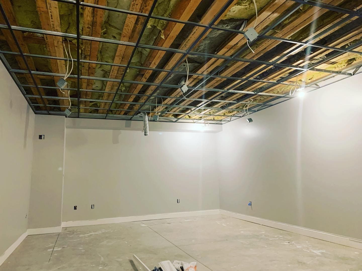 Ceiling with wood beams, exposed wiring, and insulated panels, light gray walls, concrete floor.