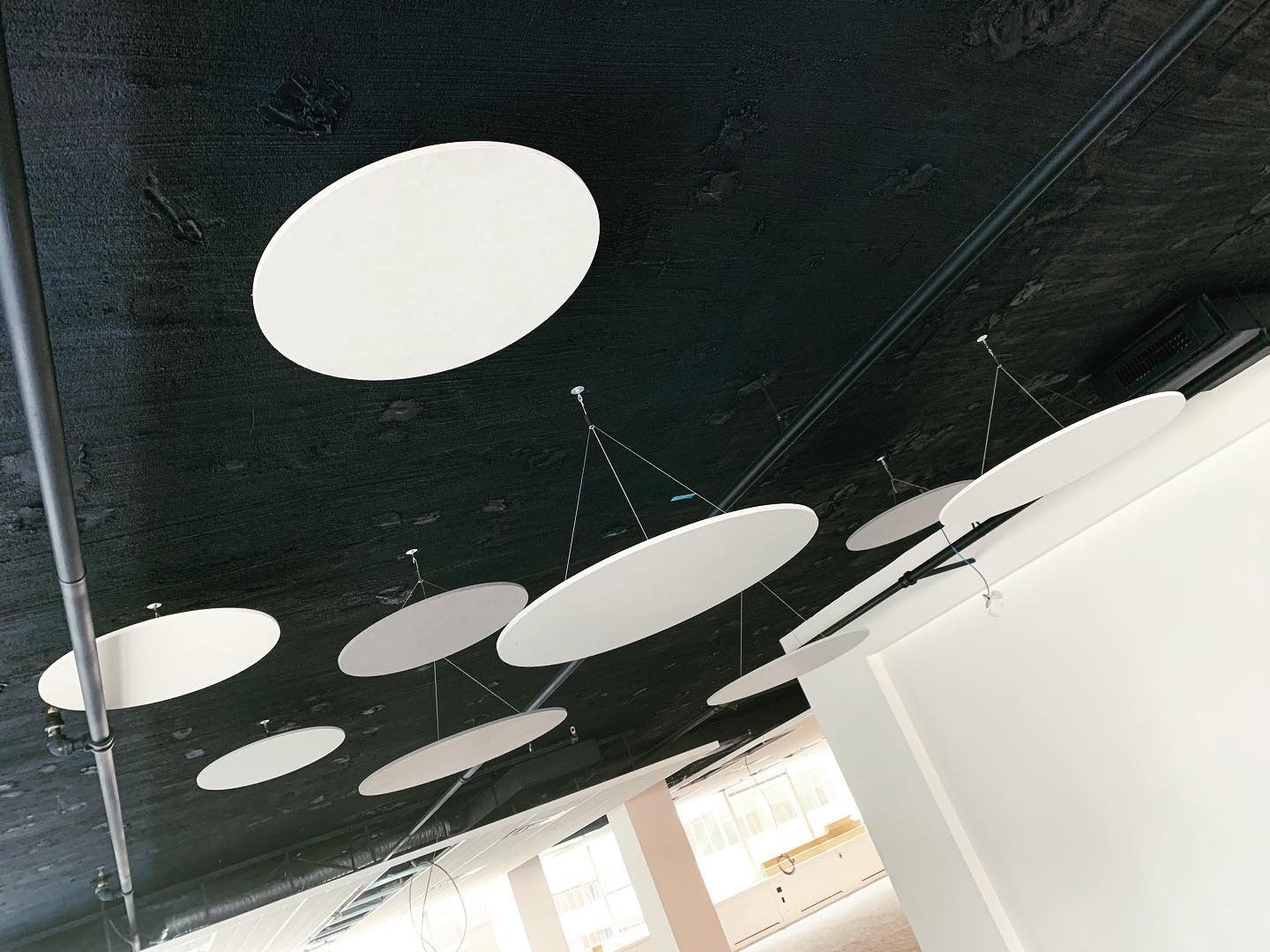 Black ceiling with hanging white circular acoustic panels.