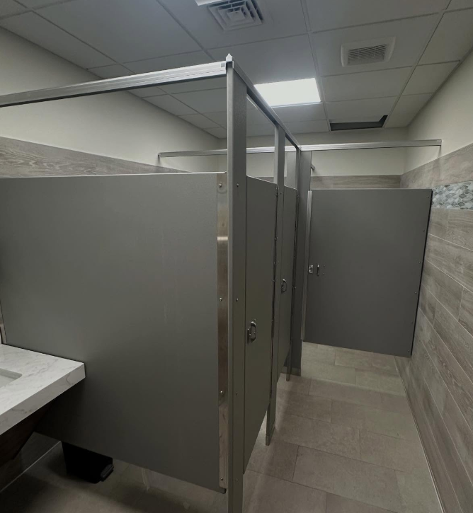 Public restroom with gray stalls, light-colored walls and floor, and a bright ceiling.