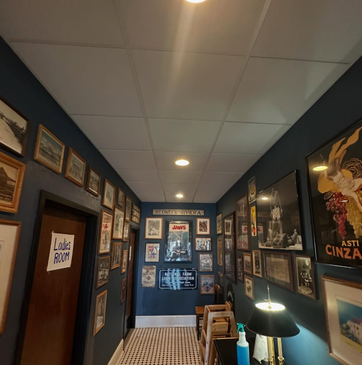 Narrow hallway with framed art on blue walls, overhead lights, and a 