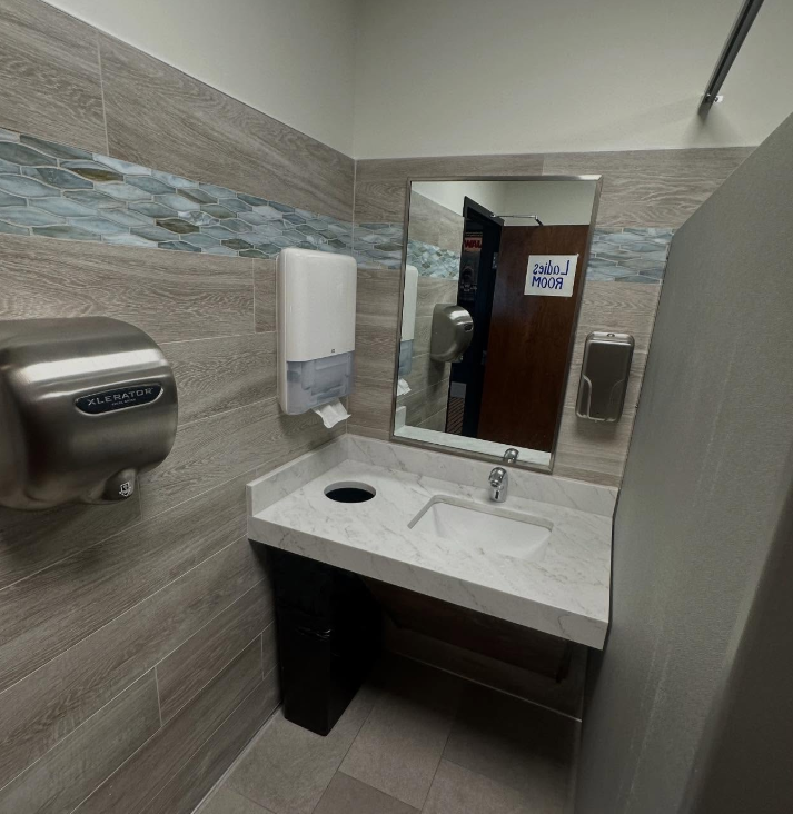 Public restroom with sink, mirror, and hand dryer. Grey tile walls.