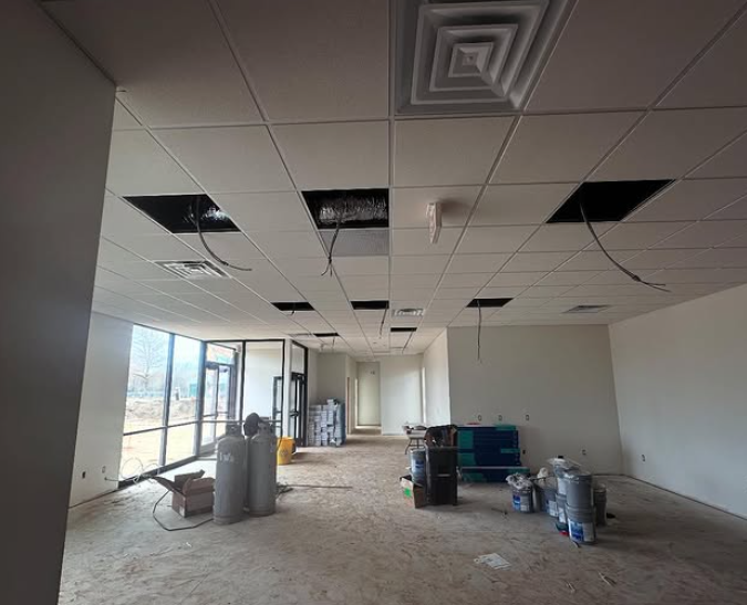Interior of a room under construction, with a drop ceiling, exposed wiring, and large windows.