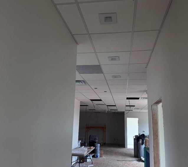 Interior view of a hallway under construction, featuring a suspended ceiling and doorways leading to unfinished rooms.