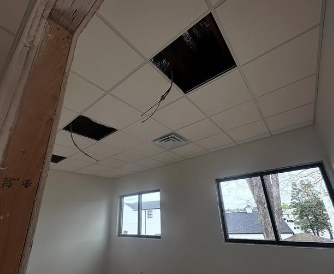 Interior room with missing ceiling tiles, two windows, and exposed wood beam.